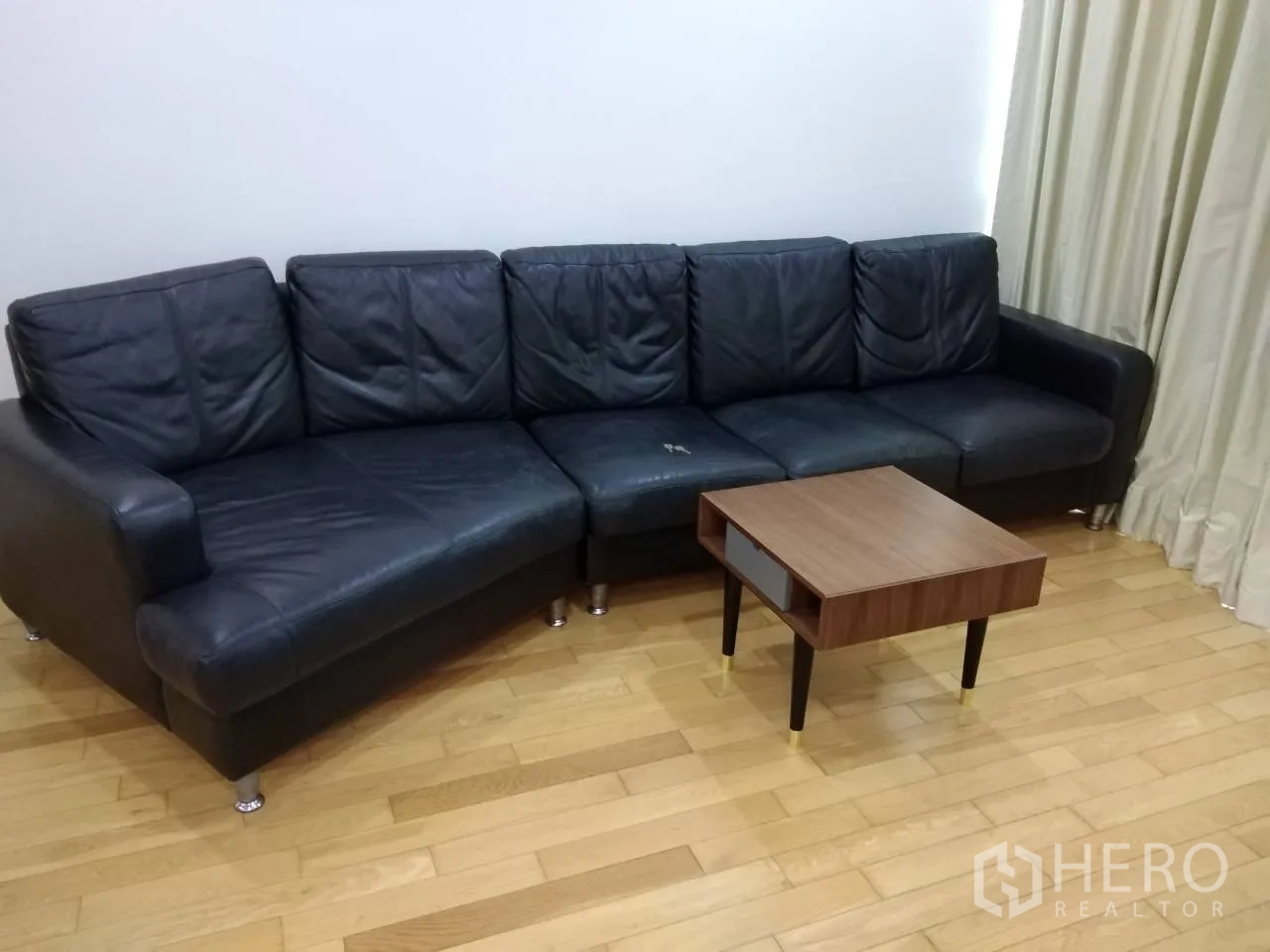 คอนโด ให้เช่าในKhlong Toei, Bangkok - โซฟาหนังทรงแอลสีดำกับโต๊ะกาแฟไม้บนพื้นไม้ขัดเงา