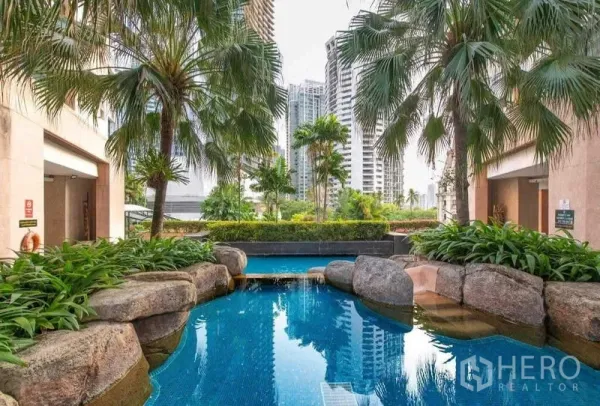 Condominium for rent in Khlong Toei, Bangkok - Tropical landscaped swimming pool with rocks and palm trees against the city skyline.