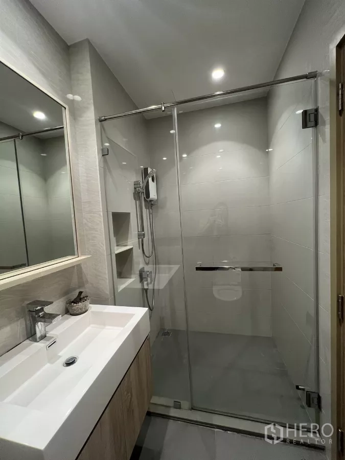 Condominium for rent or sale in Chatuchak, Bangkok - Modern bathroom with glass shower enclosure and rectangular vanity with storage.