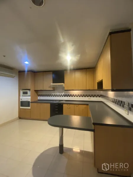 Condominium for rent or sale in Watthana, Bangkok - Large U-shaped kitchen with wood cabinetry, tiled floor, built-in oven and cooktop.