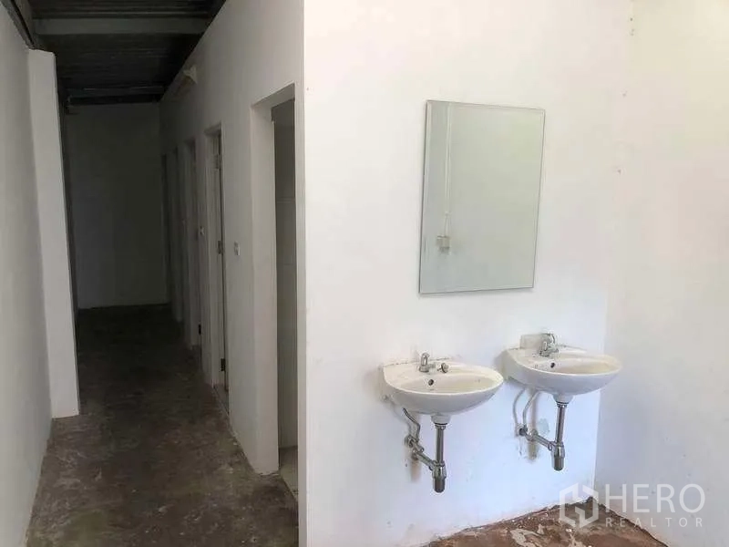 Factory for rent or sale in Bang Phli, Samut Prakan - Utility area featuring twin wall-mounted sinks next to a corridor leading to multiple washrooms.
