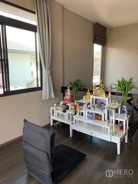 Detached House for rent or sale in Bang Phli, Samut Prakan - Bright upstairs corner with white altar shelves, floor cushion and large windows on wood flooring.