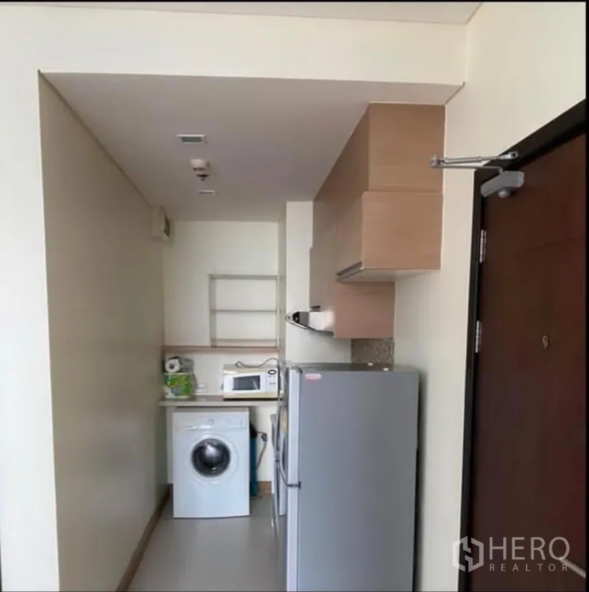 Condominium for rent in Watthana, Bangkok - Compact kitchenette with upper cabinets, fridge, microwave, and in-unit washing machine.