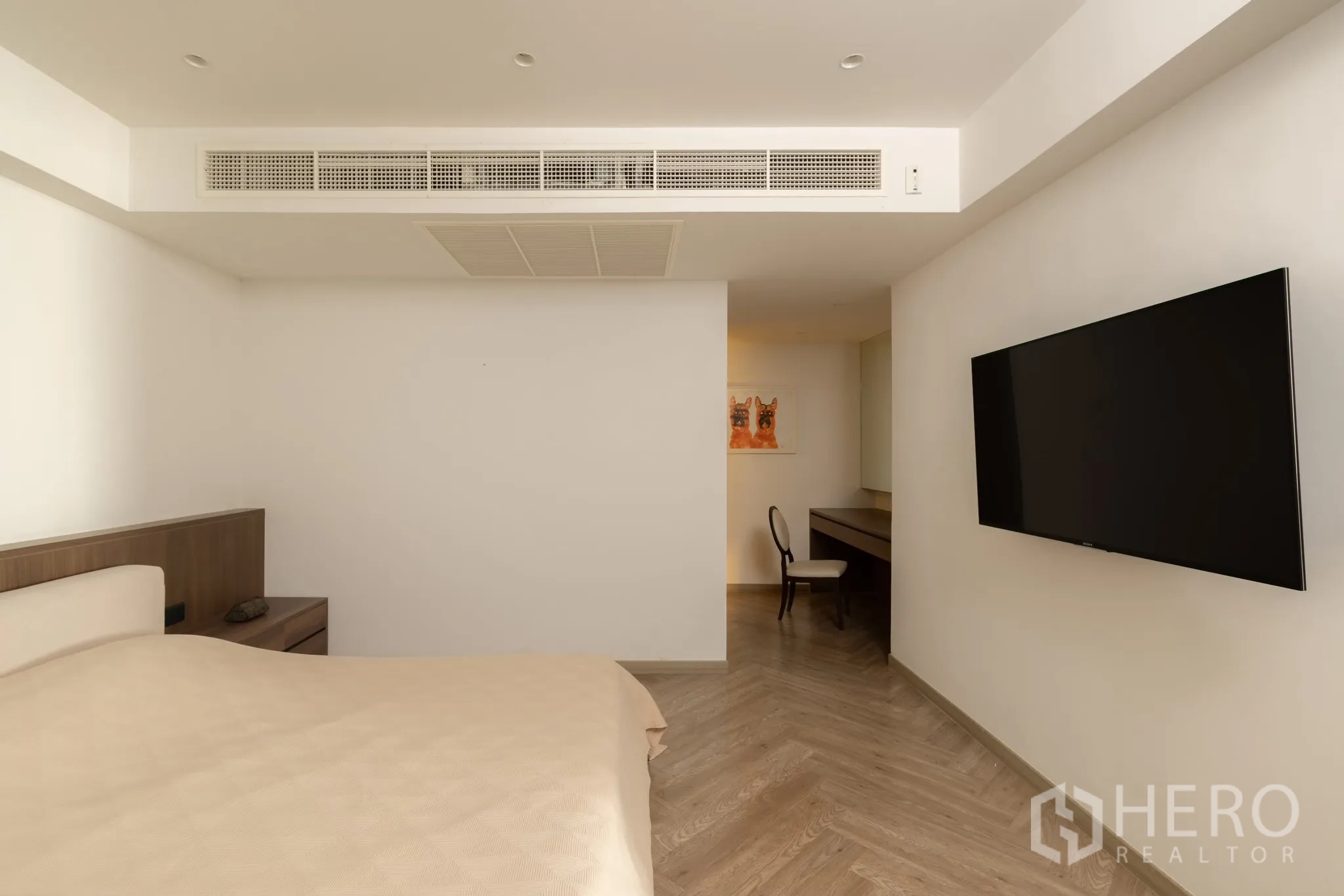 Condominium for sale in Khlong Toei, Bangkok - Second bedroom with wall‑mounted TV, work nook, built‑in air‑conditioning vent and herringbone floor.
