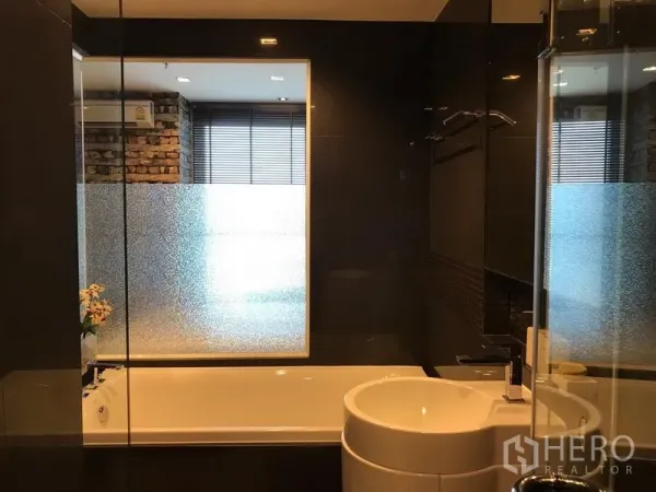 公寓 出租在Sathon, Bangkok - 浴室配浴缸、磨砂窗与圆形台盆，深色装饰