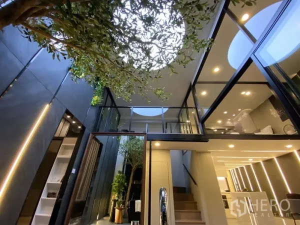 Detached House for sale in Watthana, Bangkok - Atrium with skylight above an indoor tree, glass bridges, and warm downlights.