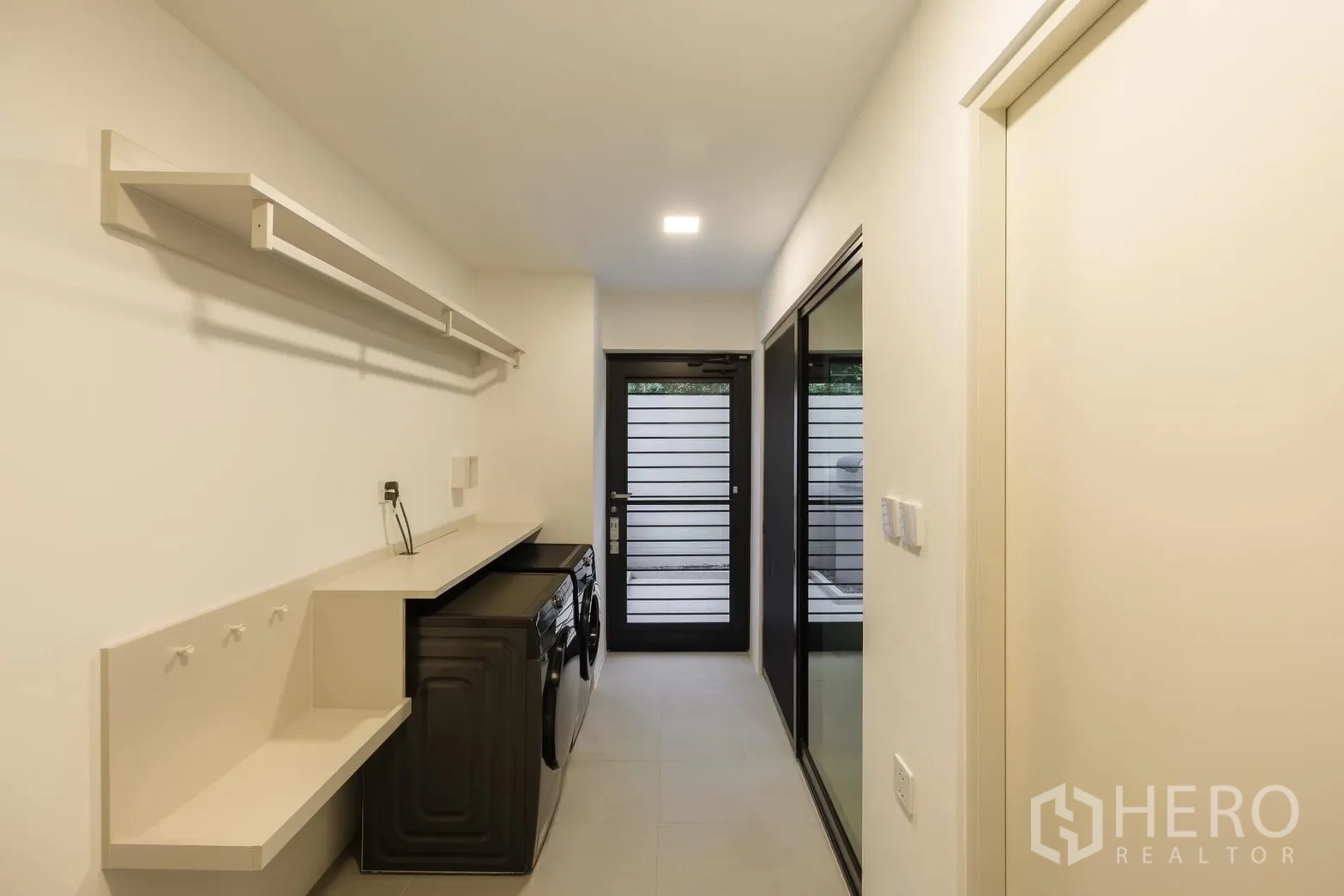 独栋房屋 for rent or sale in Saphan Sung, Bangkok - 洗衣房配有操作台、开放搁架、洗衣机与烘干机，并通向侧院的玻璃门。