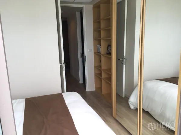 公寓 出售在Bang Rak, Bangkok - 舒适卧室，带嵌入式书架与镜面衣柜，浅色木地板。