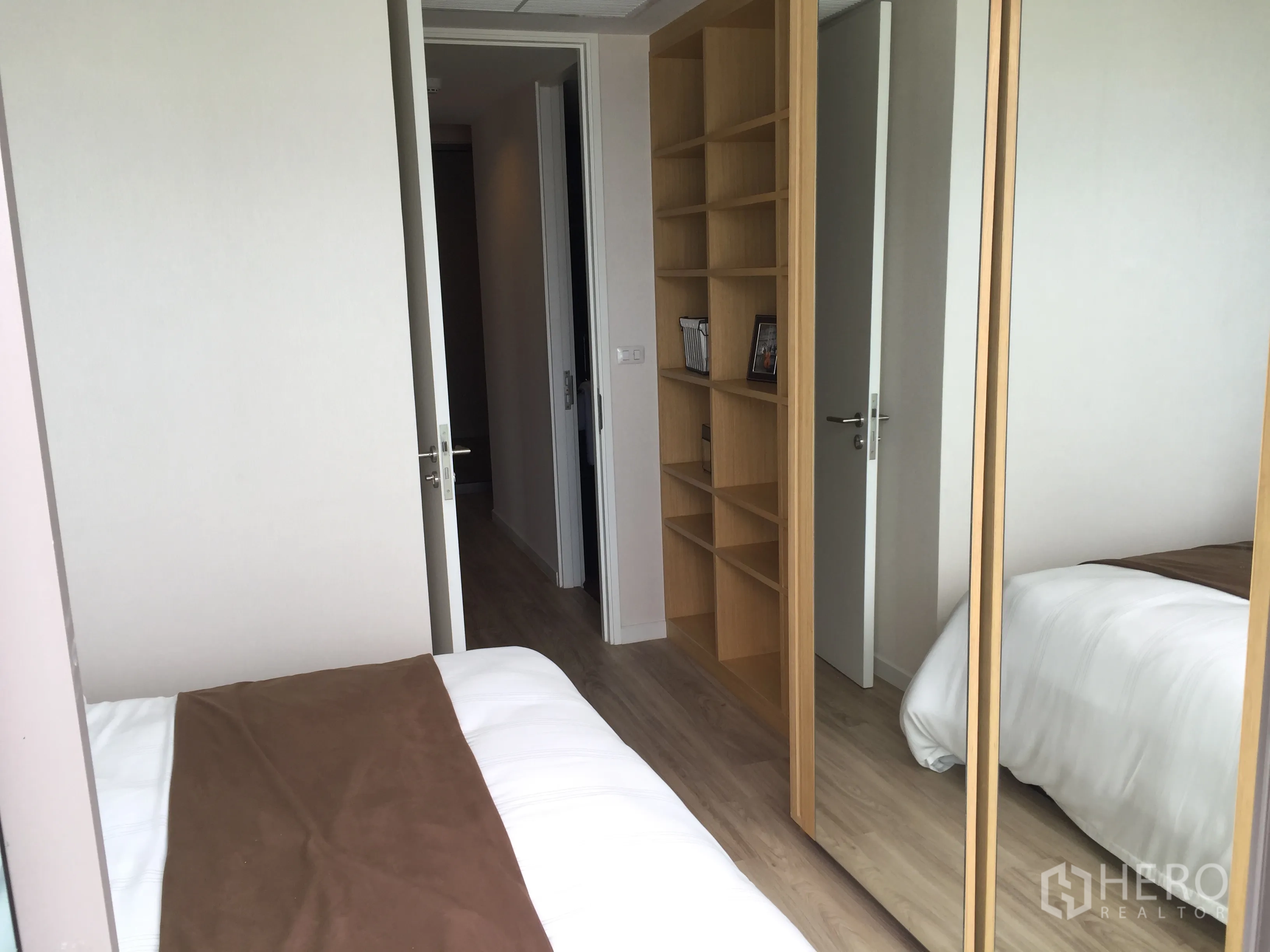 公寓 出售在Bang Rak, Bangkok - 舒适卧室，带嵌入式书架与镜面衣柜，浅色木地板。