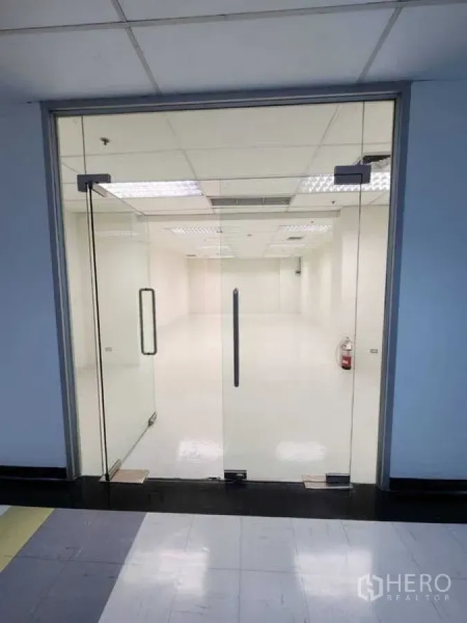 办公空间 出租在Watthana, Bangkok - 双开玻璃门入口，可见亮堂的办公室内饰、地砖与灭火器。