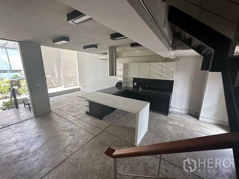 Home Office for rent in Phra Khanong, Bangkok - Open-plan kitchen with a white island, black cabinetry and concrete floors.