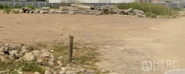 Land for sale in Lam Luk Ka, Pathum Thani - Wide open plot with gravel surface and building materials near a perimeter fence, suitable for development in Lam Luk Ka, Pathum Thani.