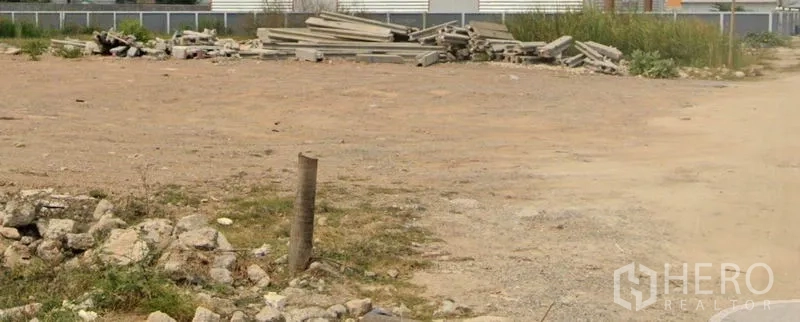 Land for sale in Lam Luk Ka, Pathum Thani - Wide open plot with gravel surface and building materials near a perimeter fence, suitable for development in Lam Luk Ka, Pathum Thani.