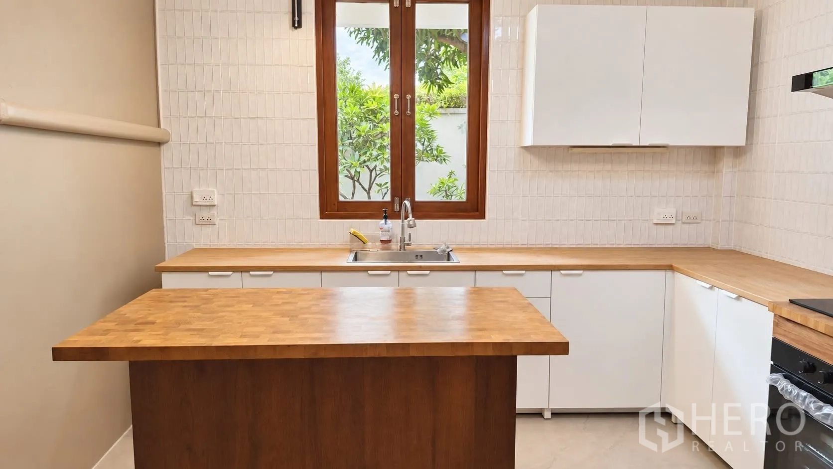 Detached House for rent in Khlong Toei, Bangkok - Modern kitchen with window, white cabinets, wooden countertops, and central island.