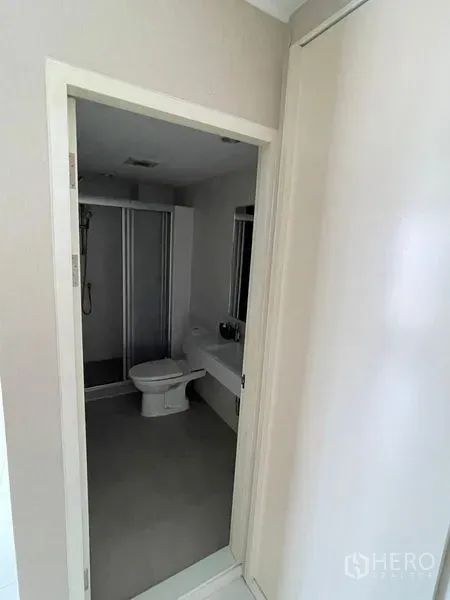 Condominium for sale in Suan Luang, Bangkok - Bright tiled bathroom with glass-enclosed shower, toilet and vanity.