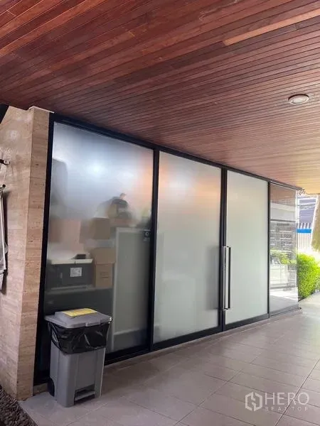 零售空间 出租在Watthana, Bangkok - 小型商铺，磨砂玻璃推拉门与长把手，位于木质顶棚走道下。