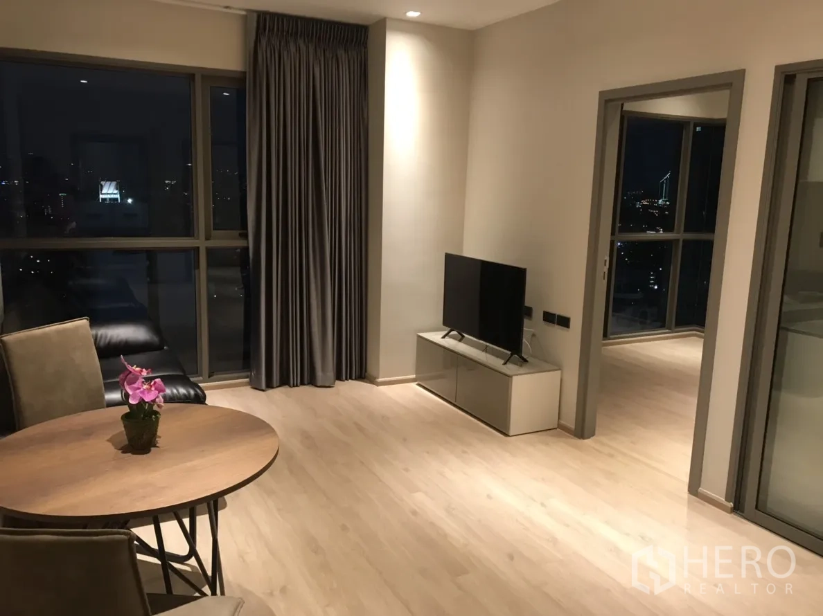 公寓 出租在Phra Khanong, Bangkok - 开放式客餐厅，浅色木地板，电视柜，落地窗俯瞰夜景。