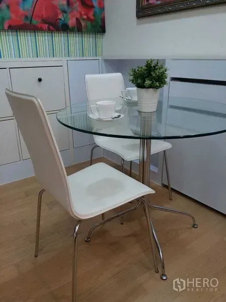 คอนโด ขายในWatthana, Bangkok - มุมทานอาหารขนาดกะทัดรัด โต๊ะกระจกกลม เก้าอี้สีขาวสองตัว และกระถางต้นไม้บนพื้นไม้.