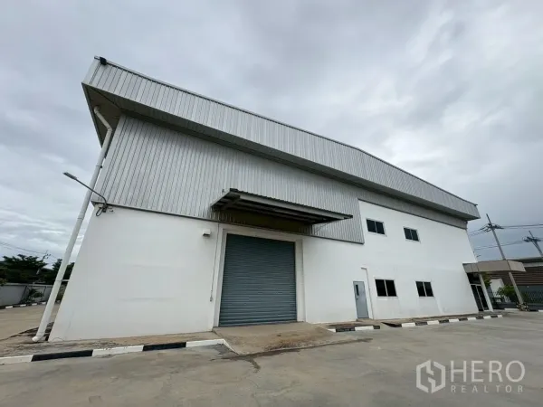 Factory for sale in Bang Bo, Samut Prakan - Warehouse facade with loading canopy and large roller door beside windows.