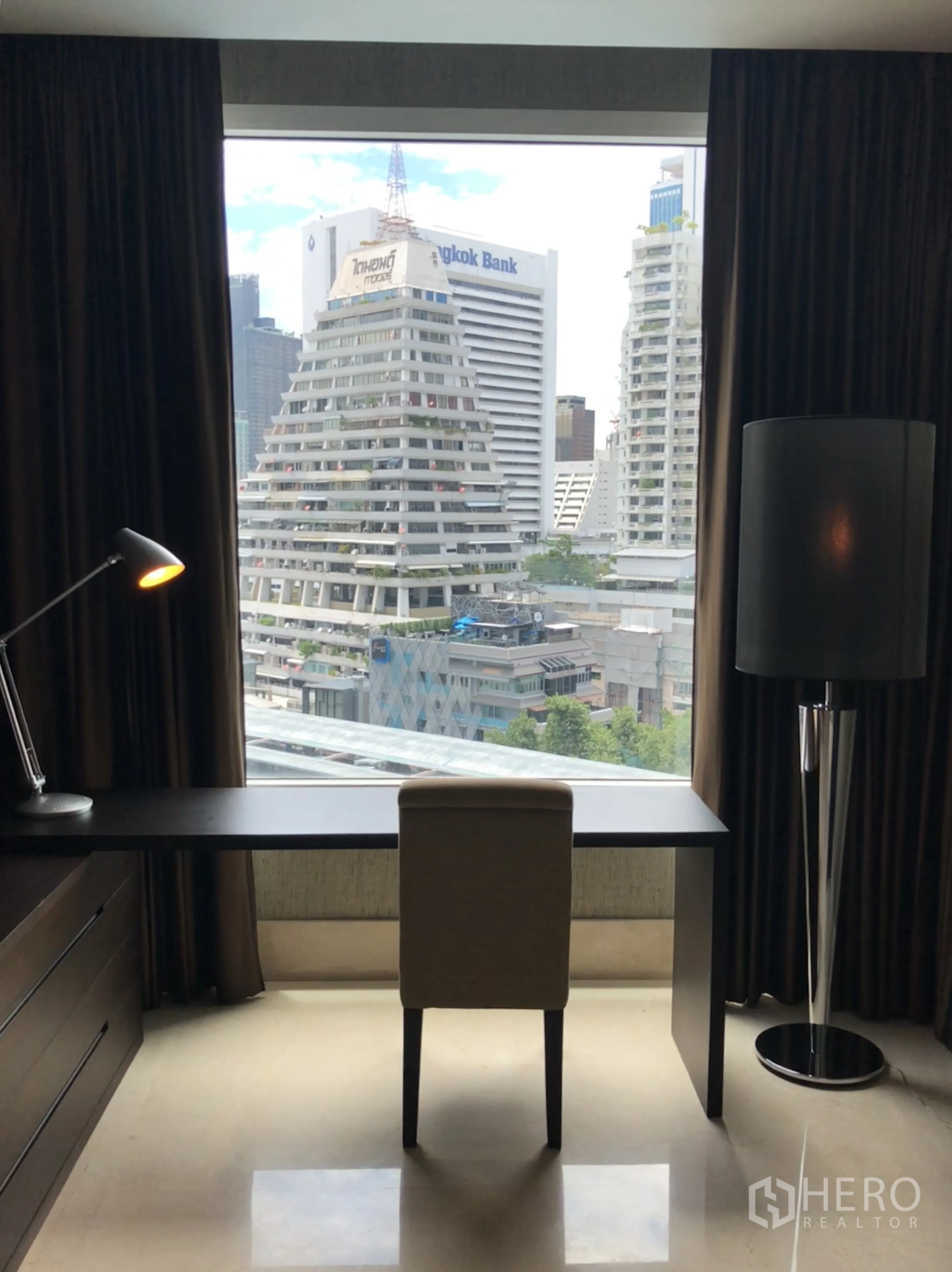 Condominium for rent in Bang Rak, Bangkok - Workstation facing a picture window with panoramic city view, desk lamp and floor lamp.