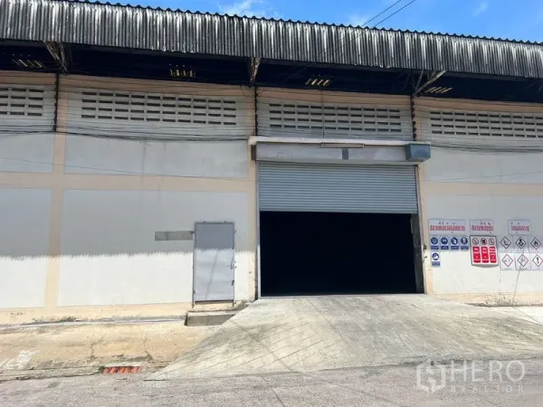 คลังสินค้า ให้เช่าในMueang Samut Prakan, Samut Prakan - ด้านหน้าโกดังพร้อมทางลาดเข้าสินค้า ประตูม้วน และป้ายความปลอดภัย