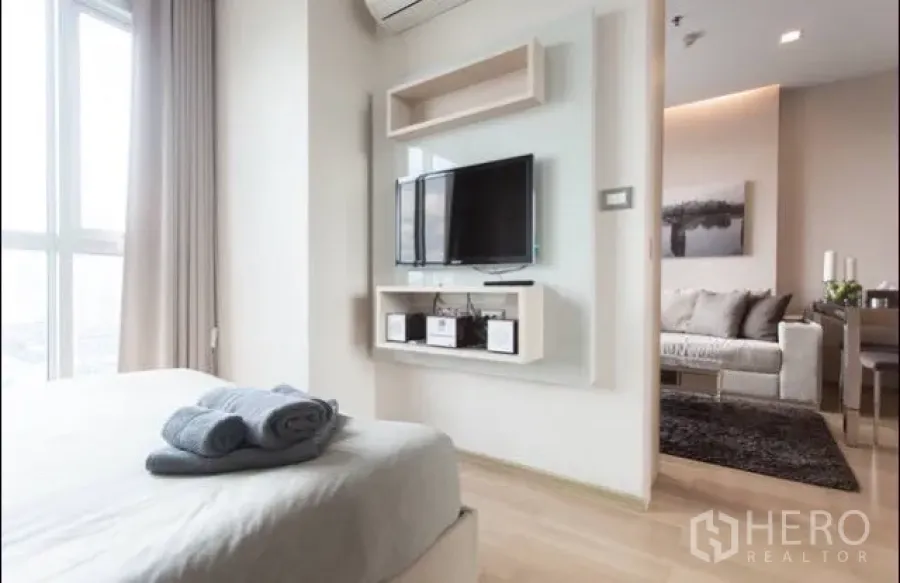 Condominium for rent in Ratchathewi, Bangkok - Ratchathewi Bangkok condo bedroom with wall-mounted TV, built-in shelving and light wood flooring opening to the living area.