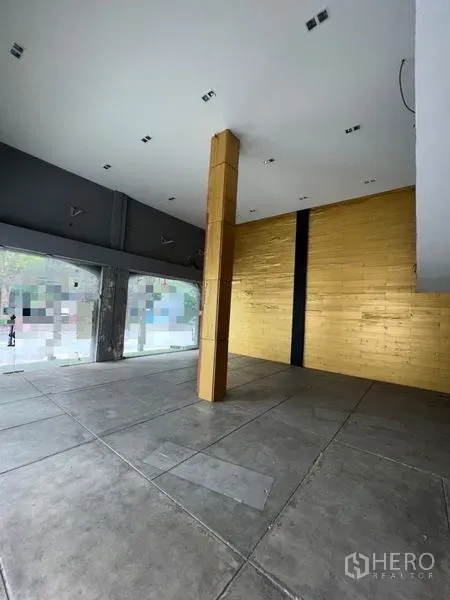 店屋 出租在Watthana, Bangkok - 挑高零售空间，水泥地面、金色特色墙与临街落地窗。