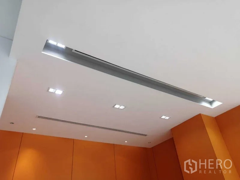 办公空间 出租在Pathum Wan, Bangkok - 橙色墙面上方的嵌灯与长条空调风口。