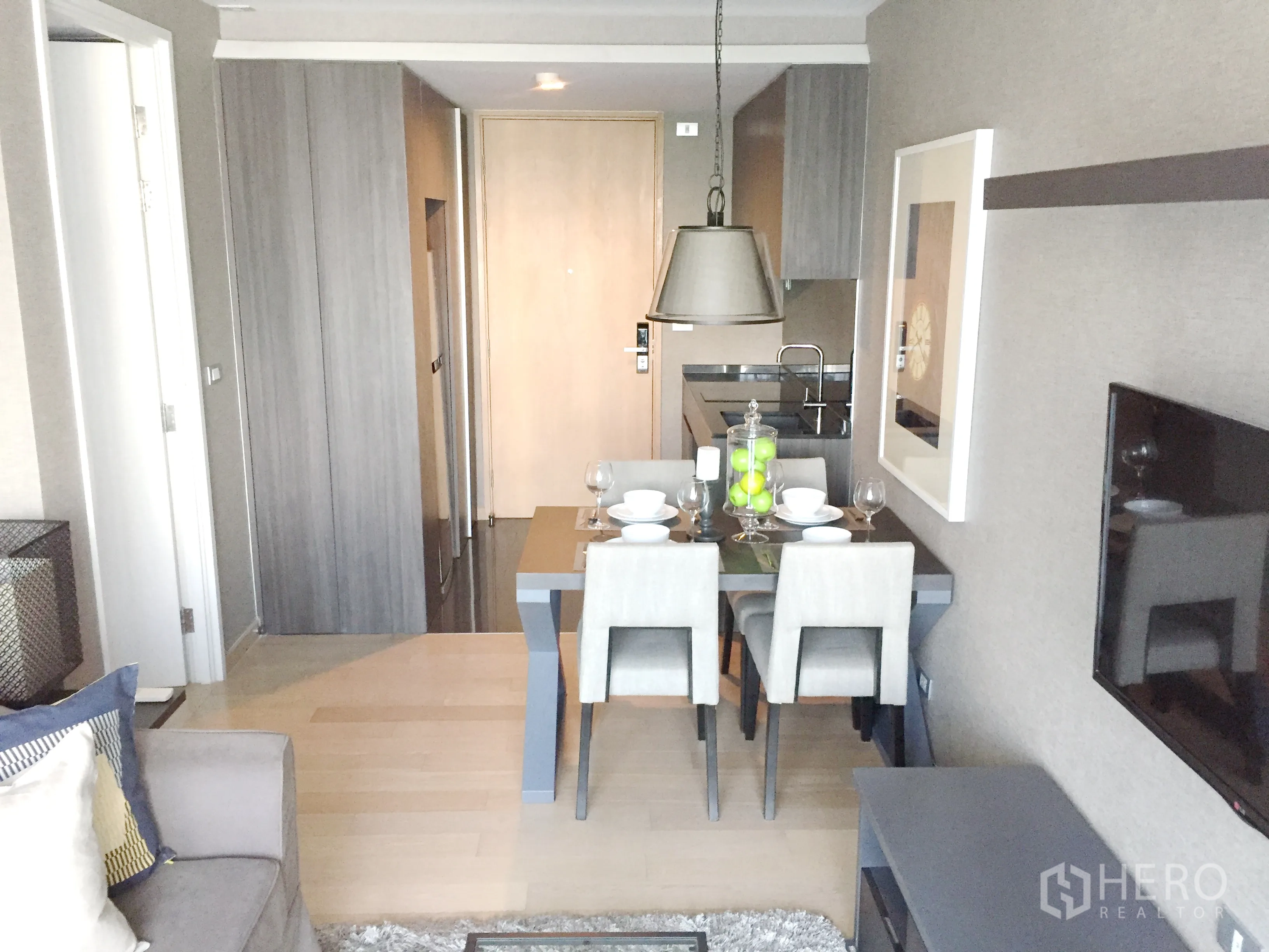 Condominium for rent in Watthana, Bangkok - Open-plan living and dining area with four-seat table, pendant light, and compact kitchen with wood cabinetry.