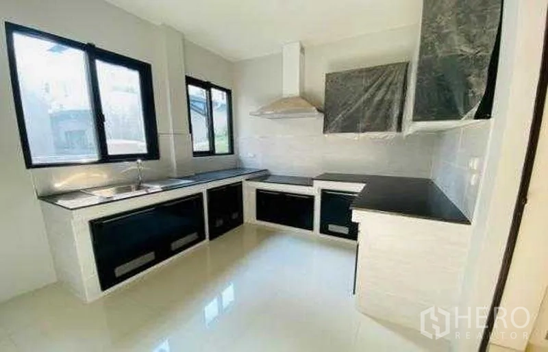 Detached House for sale in Bang Phli, Samut Prakan - Light-filled kitchen with L-shaped counters, black worktops and stainless hood.
