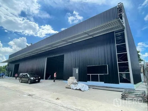 Warehouse for rent in Pak Kret, Nonthaburi - Brand-new black metal warehouse exterior with wide canopy, loading bays and parking area.