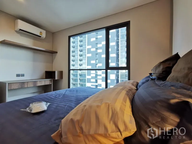 Condominium for rent in Ratchathewi, Bangkok - Bedroom with city-view window, built-in desk and shelving plus air conditioner in a Ratchathewi condo near BTS Nana.