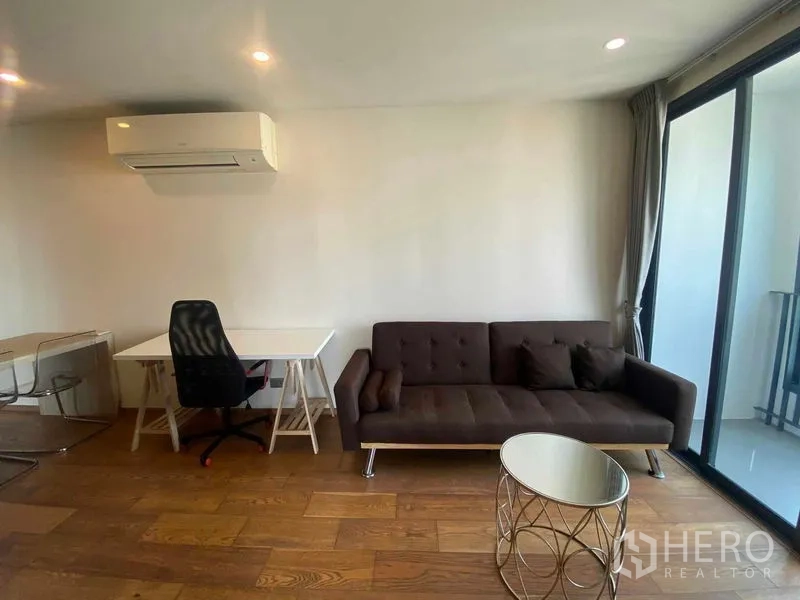 Condominium for rent or sale in Ratchathewi, Bangkok - Work corner with desk beside a sofa and glass doors to the balcony.