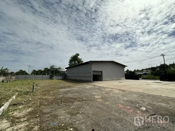 Warehouse for rent in Min Buri, Bangkok - Side angle of the warehouse showing an expansive yard and boundary wall for truck maneuvering.