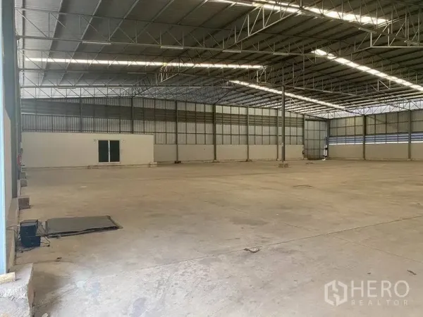 Warehouse for rent in Lat Krabang, Bangkok - Spacious warehouse interior with high steel truss roof, concrete floor and a small office room.