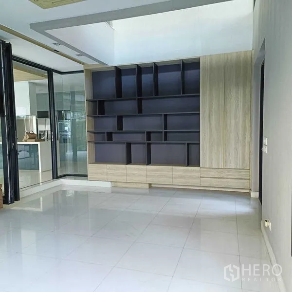 独立式住宅 出租或出售在Mueang Nonthaburi, Nonthaburi - 起居区配定制书架墙与折叠玻璃门。