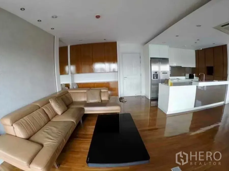 Condominium for rent or sale in Khlong San, Bangkok - Open-plan living and kitchen zone with tan sofa and glossy hardwood floors.