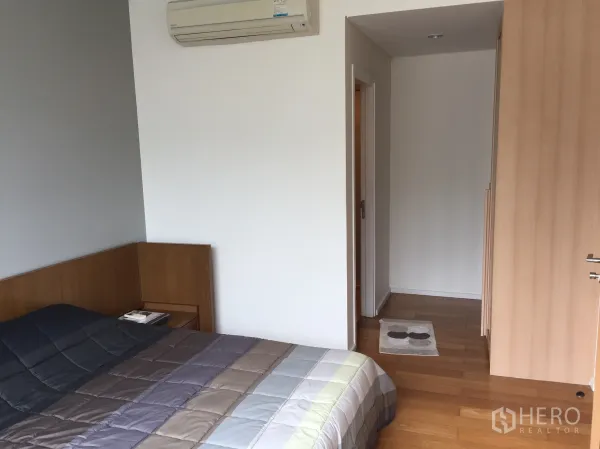 Condominium for sale in Watthana, Bangkok - Bedroom with air conditioning, built-in wardrobe, wood floors, and doorway to the bathroom.