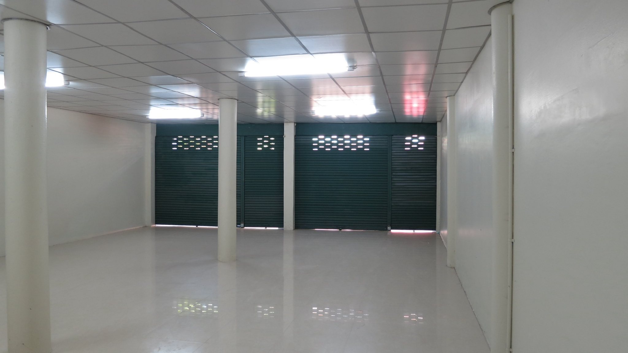 Warehouse for rent in Wang Thonglang, Bangkok - Ground-floor storage or showroom area with multiple metal roller shutters and fluorescent lighting.