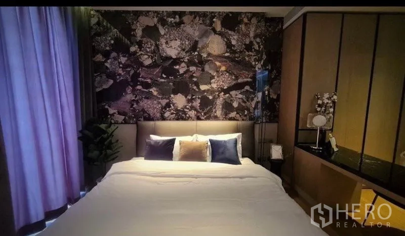 คอนโด ให้เช่าในKhlong Toei, Bangkok - ห้องนอนยามค่ำ เน้นผนังหัวเตียงลายหิน ไฟนุ่ม และเตียงปูผ้าขาวเรียบ