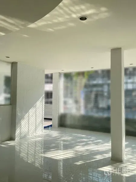 Shophouse for rent in Dusit, Bangkok - Bright open‑plan interior with glossy white tiles, columns, recessed lighting and full‑height windows.