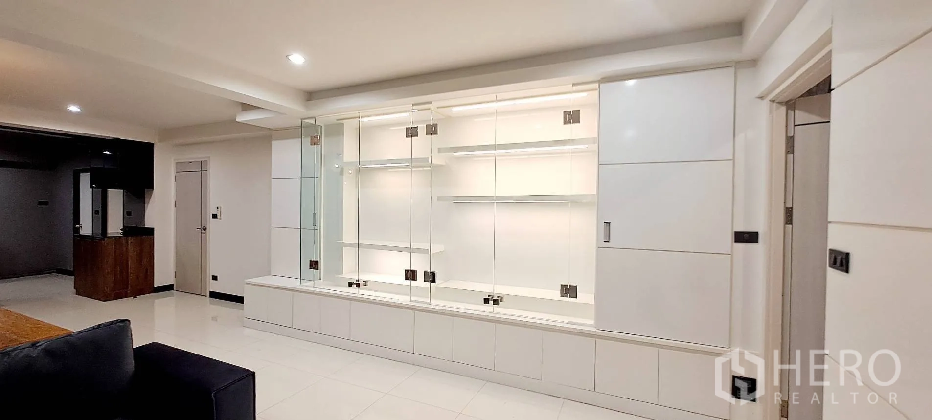 Apartment for rent in Phra Khanong, Bangkok - Built-in glass display cabinet along the living room wall.