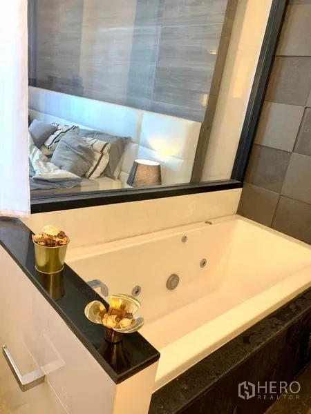 Condominium for rent or sale in Huai Khwang, Bangkok - Deep soaking bathtub beside a glass window connecting to the bedroom.