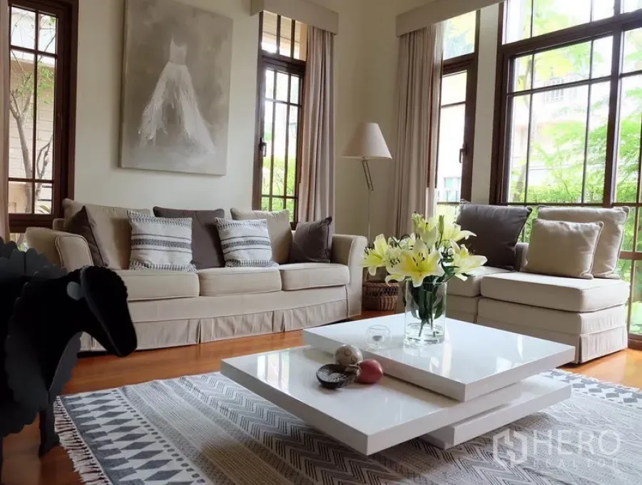 Detached House for rent in Watthana, Bangkok - Bright living room with beige sofas, white layered coffee table, large wood-framed windows and garden views.