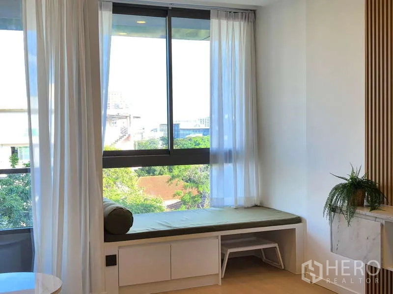 อพาร์ทเมนท์ ให้เช่า - มุมนั่งข้างหน้าต่างบานใหญ่ มองเห็นวิวสีเขียวของย่าน
