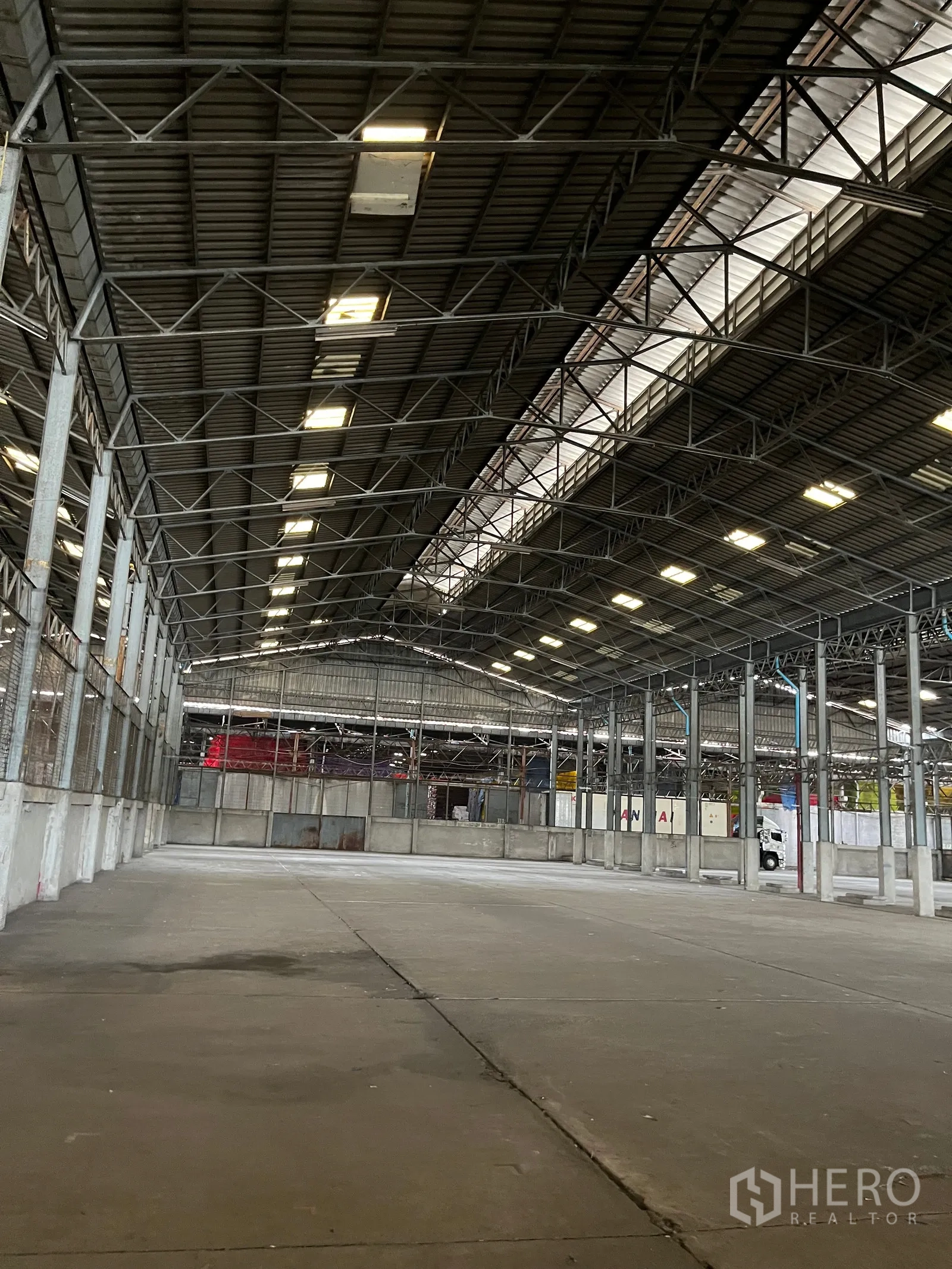 Warehouse for rent in Rat Burana, Bangkok - Open warehouse interior with high steel truss roof, skylight panels, and concrete floor.