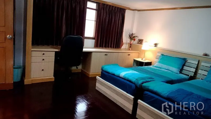Townhouse for rent in Khlong Toei, Bangkok - Twin bedroom with two single beds, long built‑in study desk, chair and dark curtains.