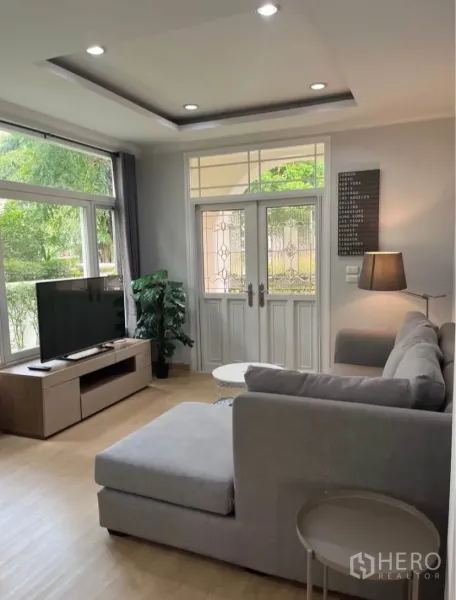 独立式住宅 出租或出售在Lat Phrao, Bangkok - 明亮客厅，转角沙发、电视柜与大窗，玻璃双开门采光充足。