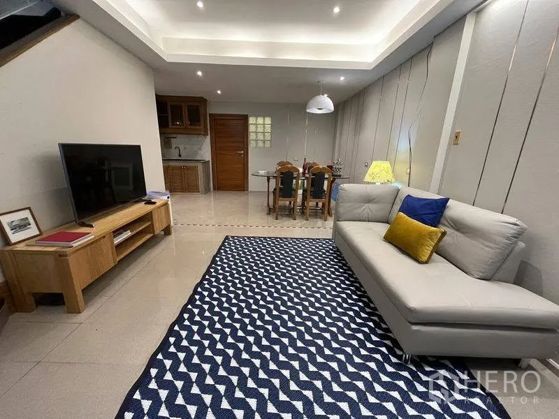 联排别墅 for rent in Phra Khanong, Bangkok - 开放式起居区，设沙发、电视柜、餐桌与花纹地毯。