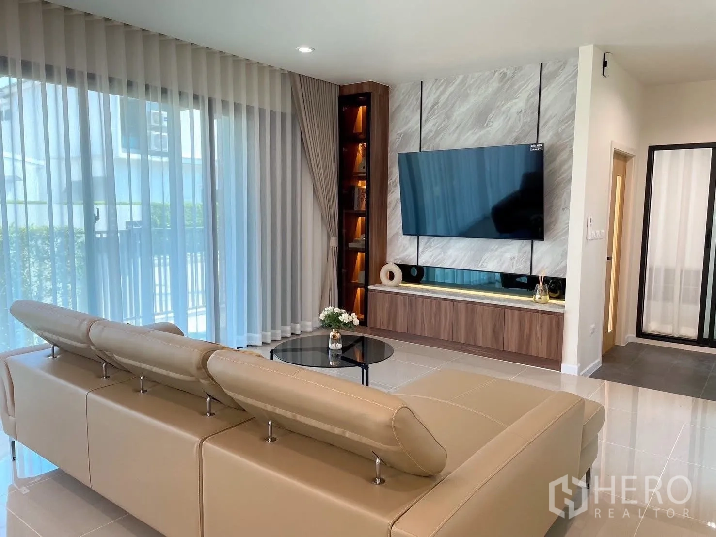 Detached House for rent in Bang Phli, Samut Prakan - Contemporary living room with L-shaped leather sofa, TV on marble feature wall and sheer drapes.